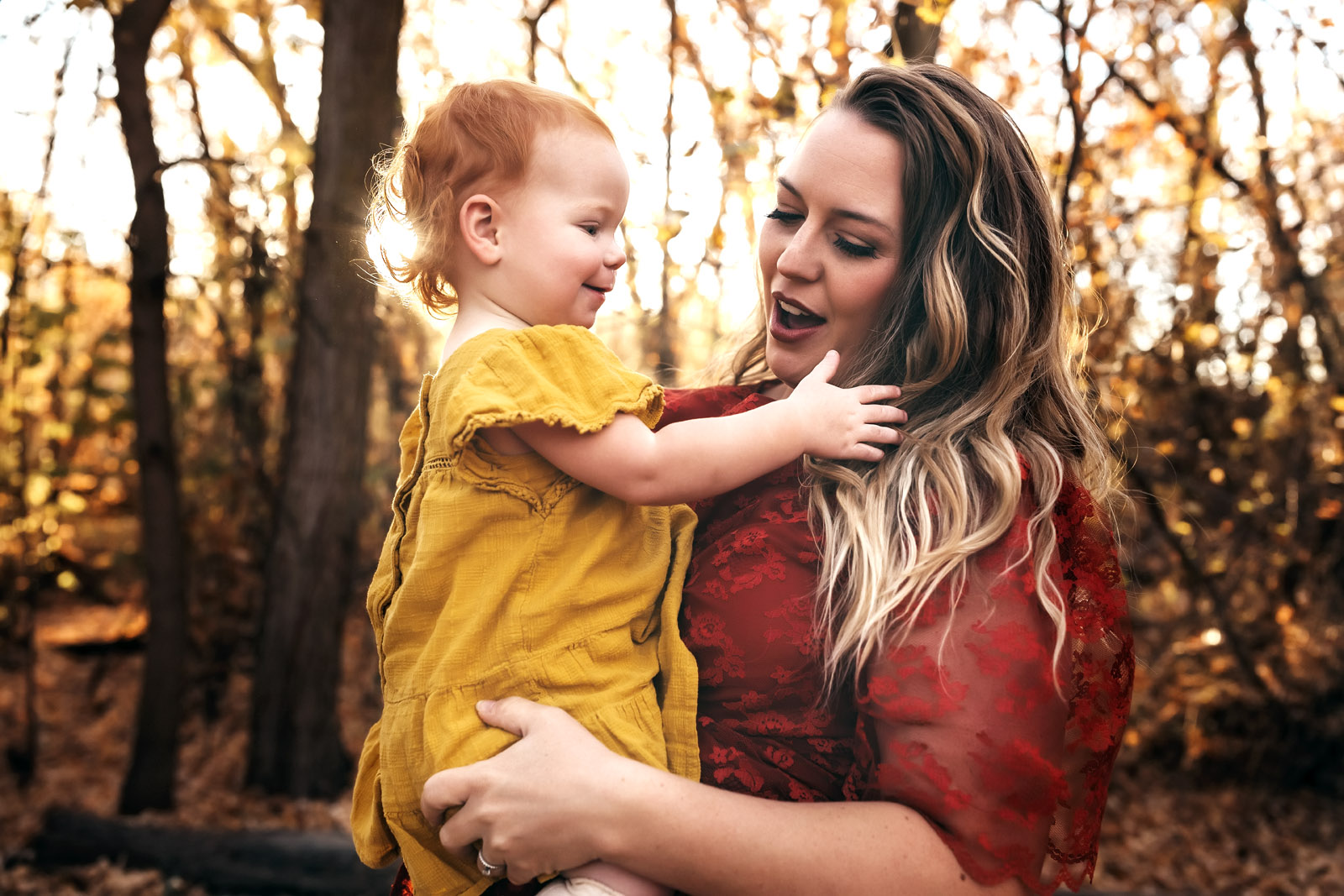 Mom wearing red dress holding baby girl with red hair and yellow dress who is touching mom's hair