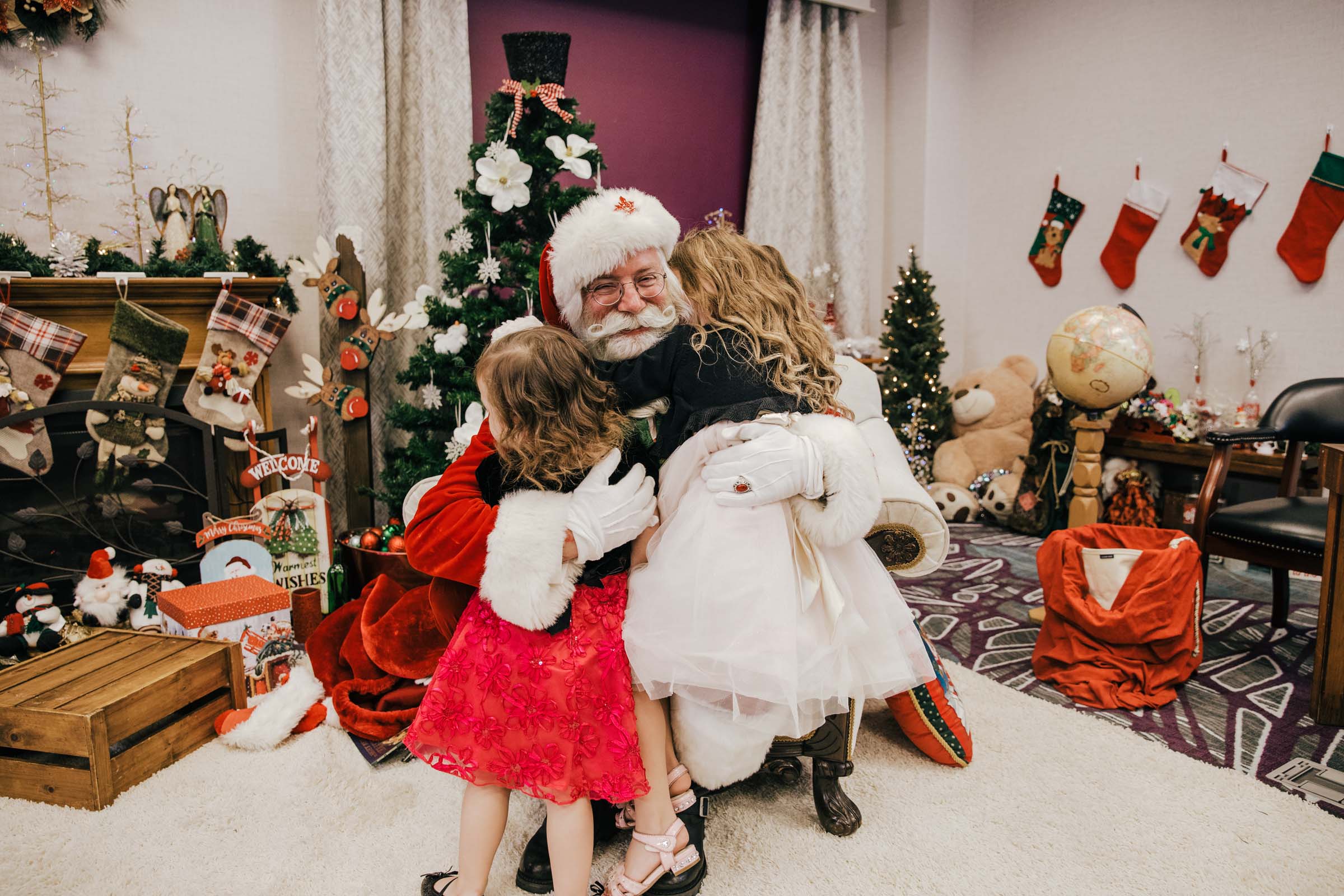 two little girls giving Santa a huge hug and Santa grinning