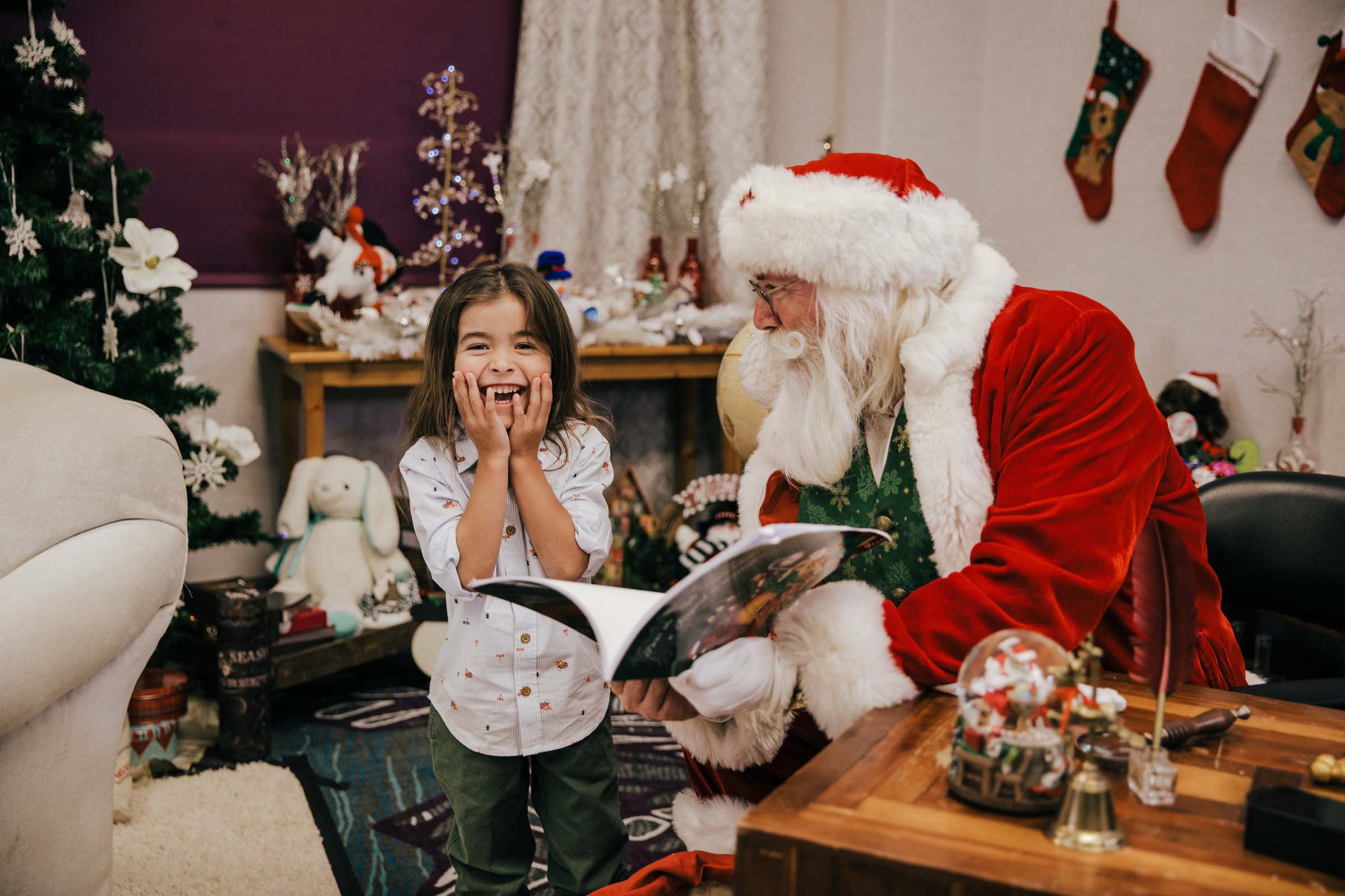 Santa Experience little boy with long dark hair grinning with Santa showing him a book