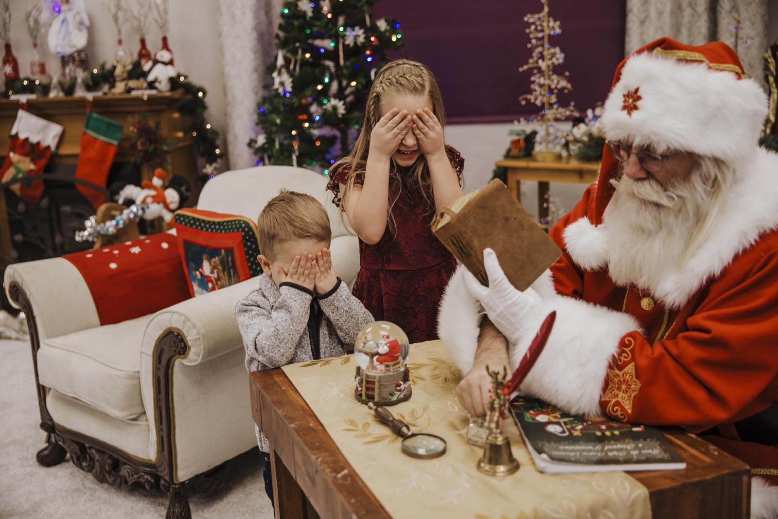 boise Santa pictures brother and sister covering their eyes while Santa is about to show them the nice list