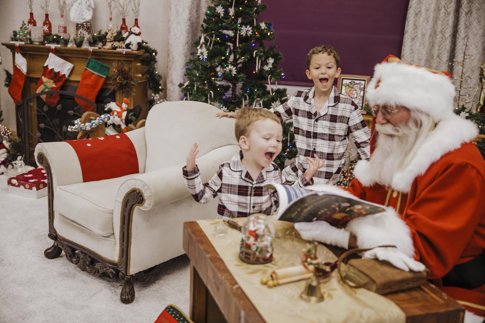 two boys in plaid pajamas smiling and laughing in glee looking at santa's magic book