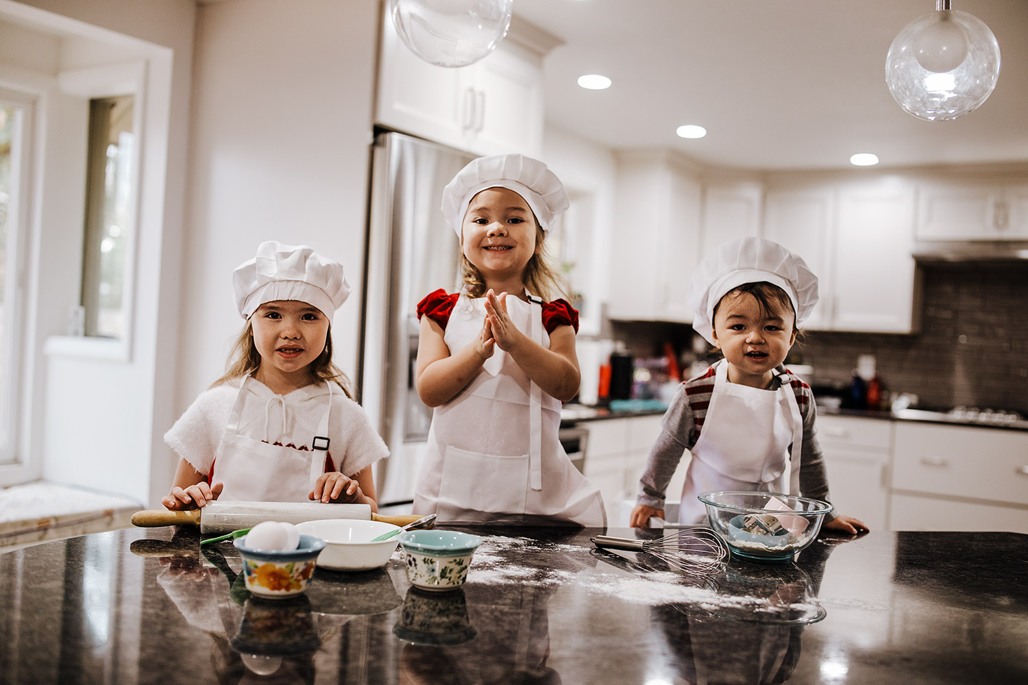 two sisters and brother wearing chef hats and aprons baking in a kitchen