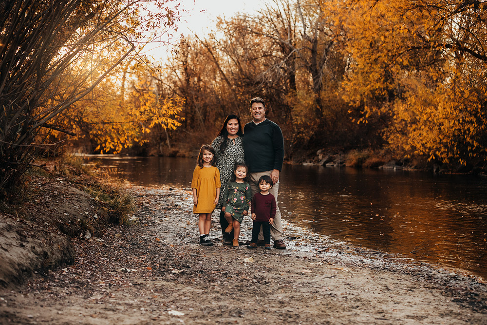 family of five standing by the river smiling in the fall time