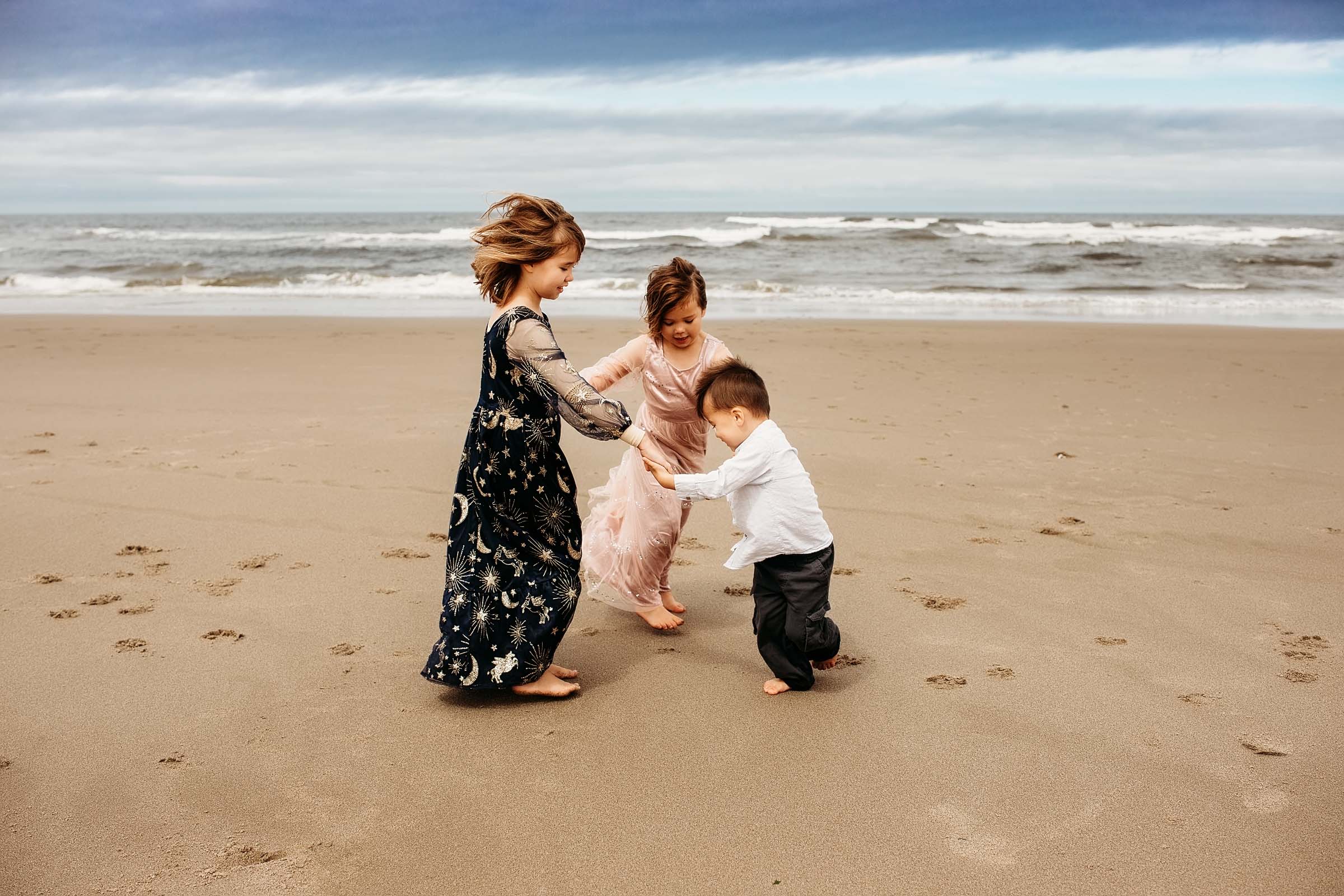 big sister, little sister, and little brother holding hands in a circle on the beach on the Oregon Coast